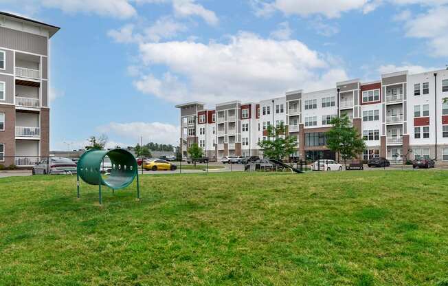 A playground with a green slide in the foreground and apartment buildings in the background.