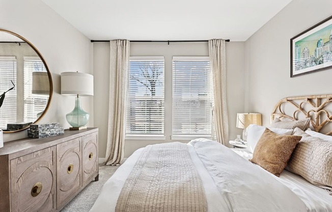 A bedroom with a large bed, a dresser with a mirror, and a window with blinds.