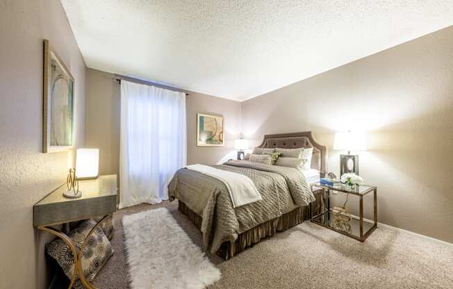 Model bedroom with large bed and dresser at Hillside Creek Apartments in Austin, TX