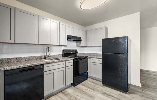 A black refrigerator stands in a kitchen with white cabinets and a black stove.