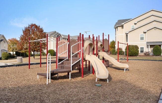 A playground with a red slide and a brown bench.