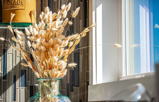 a glass vase filled with wheat in front of a window