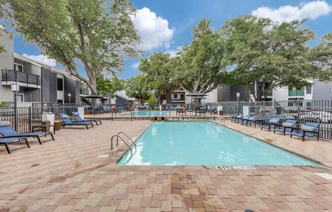 A large outdoor pool surrounded by trees and chairs.