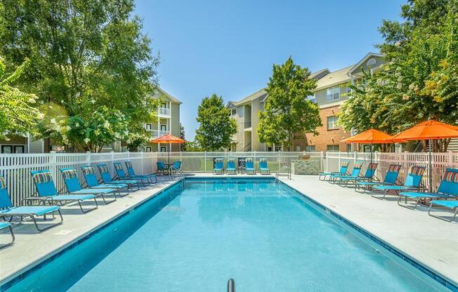 a swimming pool with blue chairs and orange umbrellas in front of a building