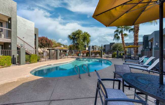 A pool area with a blue pool, sun loungers and a yellow umbrella.