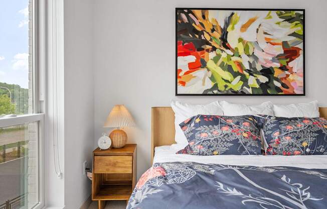 A bedroom with a large painting on the wall and a bed with a blue comforter.