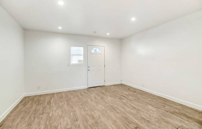 a living room with white walls and wood flooring and a white door