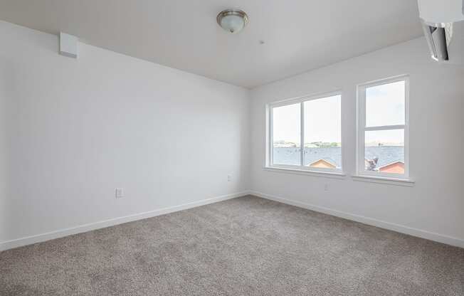 an empty living room with three windows and carpeting