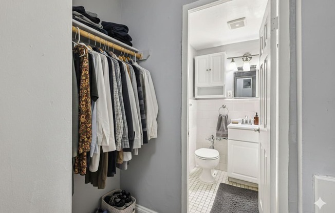 A bathroom with a toilet, sink, and a rack of clothes.