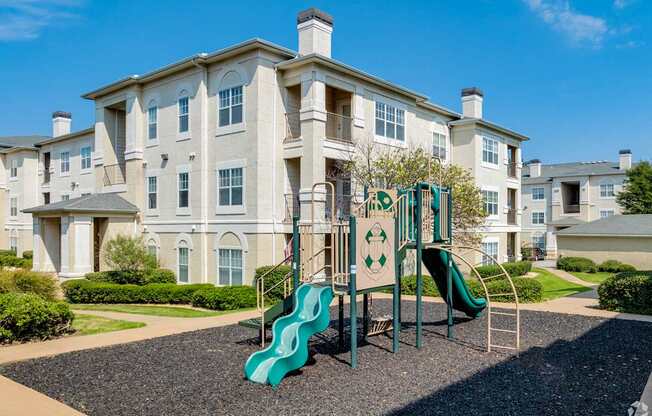 A playground with a green slide in front of a large building.