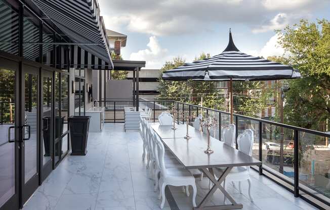 a long white patio table with chairs and an umbrella on a balcony