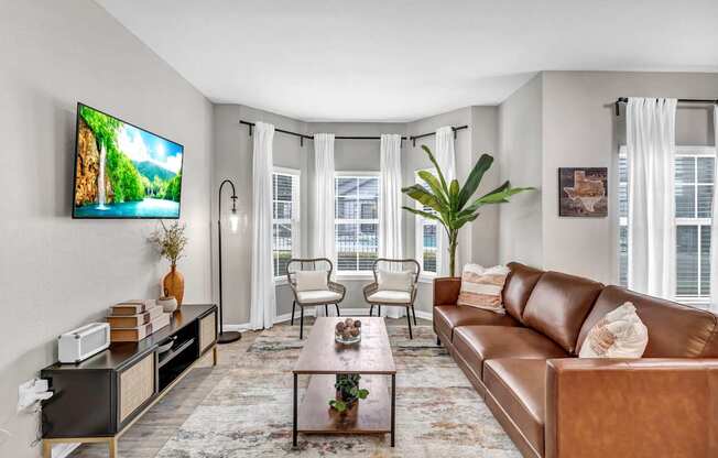 A living room with a brown leather couch, a coffee table, and a flat screen TV mounted on the wall.