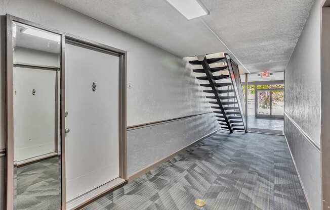 A hallway with a staircase on the right and a door on the left.