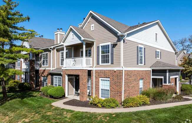 A large house with a grey roof and a brick base with a small garden in front.