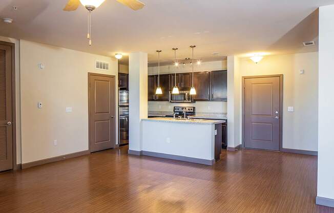 an empty living room with a kitchen in the background