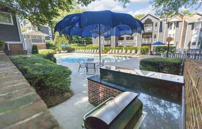 A pool area with a blue umbrella and a brick wall.