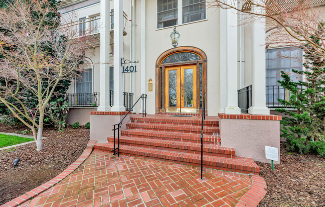 A white house with a brown door and a brick pathway leading to it.