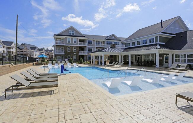 a large swimming pool with lounge chairs and a building in the background