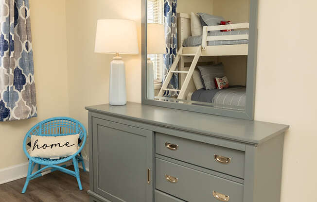 A grey dresser with a mirror and a blue chair with the word home on it.