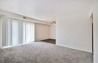 Spacious living room with large windows, neutral walls, and plush carpet at Warren Woods Apartments in Warren, MI.