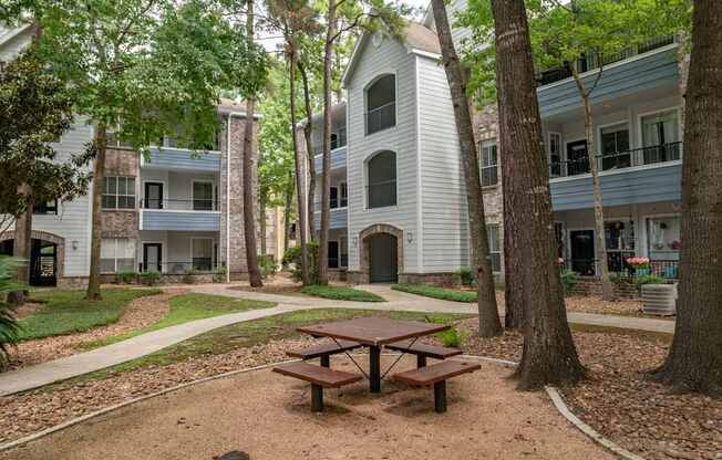 A picnic table sits in the middle of a dirt area with a building in the background.