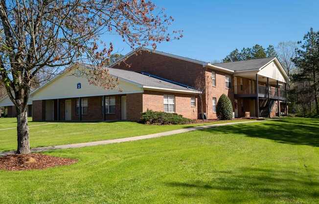 A tree with brown leaves stands in front of a building with a yellow roof.