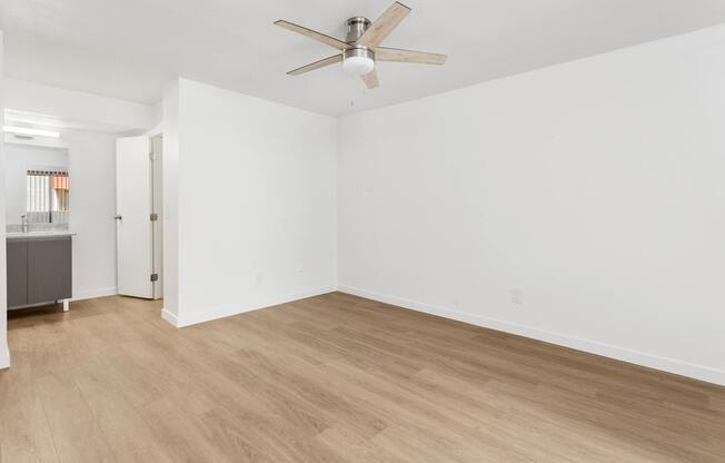 A room with a ceiling fan and light, hardwood floors, and white walls.