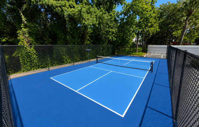 A blue pickleball court surrounded by a fence.