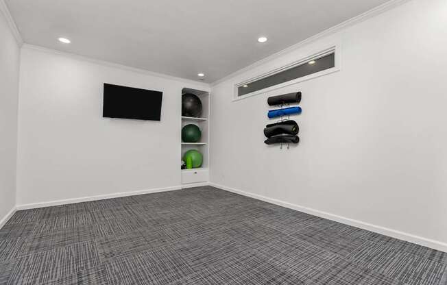 A room with a black screen on the wall and a row of exercise balls and weights on the wall.