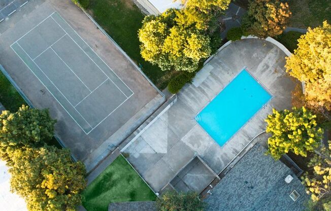 arial view of a tennis court and a pool in a backyard with trees