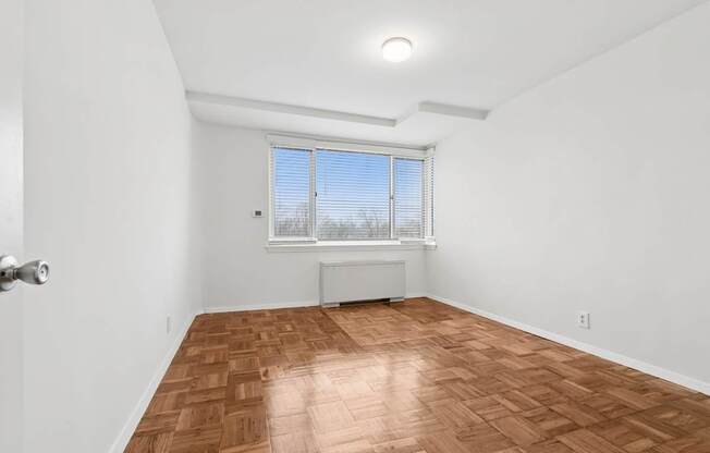 A room with a wooden floor and a window with blinds.