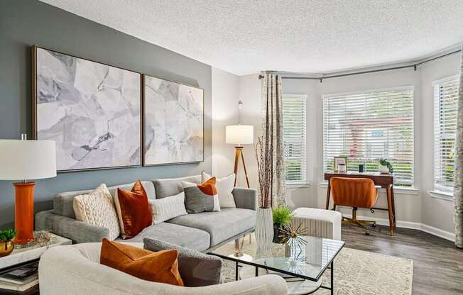A living room with a grey couch, a glass table, and a painting on the wall.