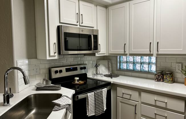 Kitchen with white cabinets and black oven range with microwave above it.