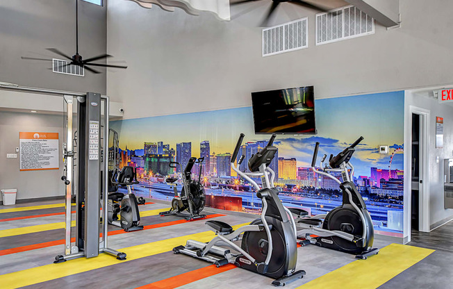 a gym with cardio equipment and a mural of a city on the wall