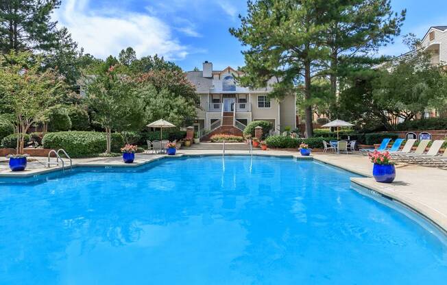 A large blue swimming pool surrounded by trees and lounge chairs.