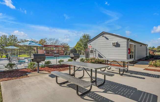 A picnic table is in the foreground of a sunny day with a pool and a building in the background.