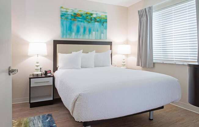 a bedroom with a white bed and a painting on the wall at Parks Residential - Denver, Colorado, 80111