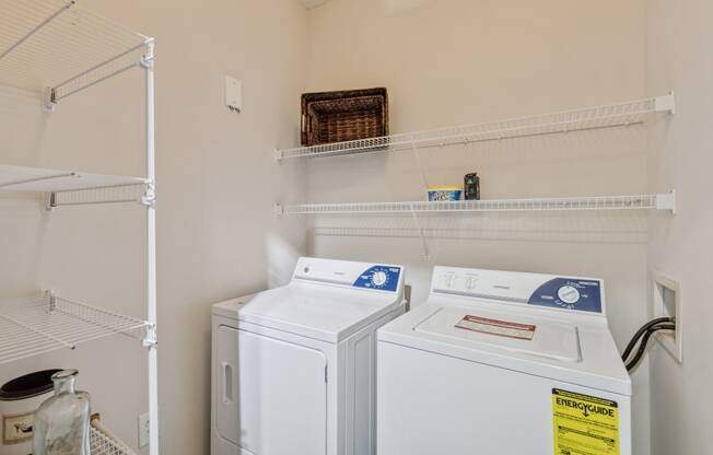 the laundry room has two washes and a dryer in it and shelves above