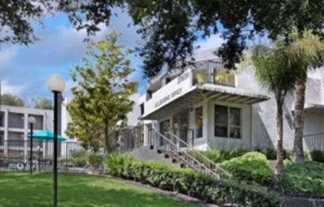 A white building with a green awning is surrounded by trees and bushes.