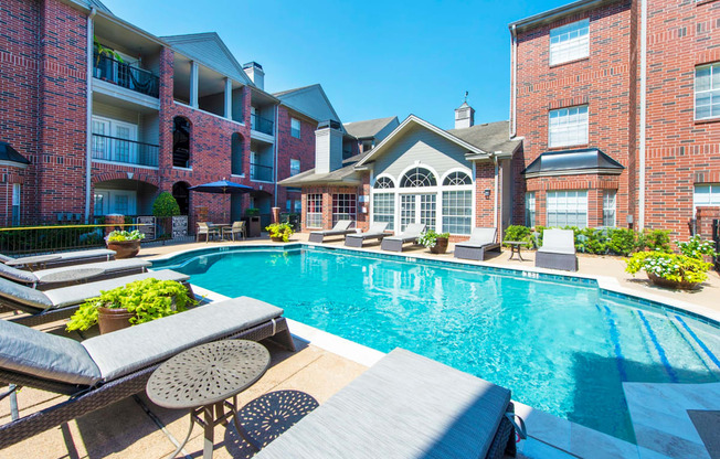 A swimming pool surrounded by lounge chairs and plants at The Inverness Apartments in Houston, TX