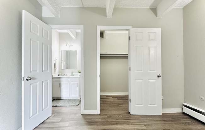 Bright and inviting bedroom featuring an open door leading to a modern bathroom, ample closet space, and elegant hardwood flooring.