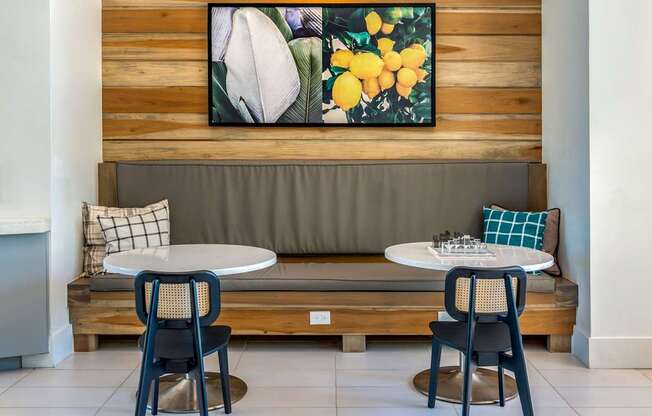 A wooden bench with a grey cushion and a painting of flowers above it.