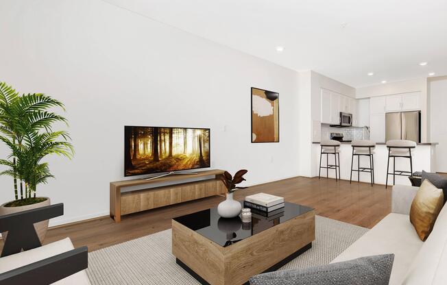 A modern living room featuring a stylish coffee table, a flat-screen TV displaying a forest scene, a soft-colored sofa with cushions, a small decorative plant, and a kitchen area in the background with bar stools. Bright lighting enhances the inviting atmosphere.