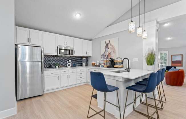 a kitchen with white cabinetry and a large white island with three blue chairs