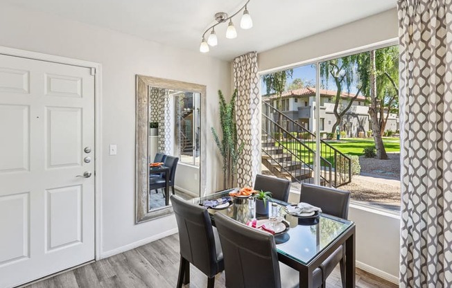A dining room with a glass table and chairs with a view of a backyard.
