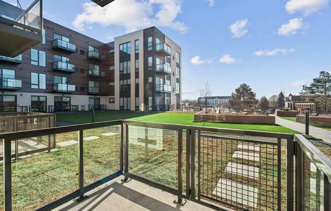 A balcony with a metal railing overlooks a grassy area and buildings.