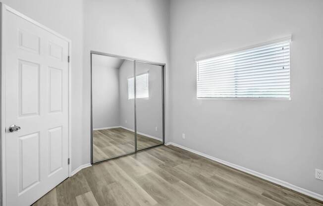 an empty bedroom with a mirrored closet door and a window