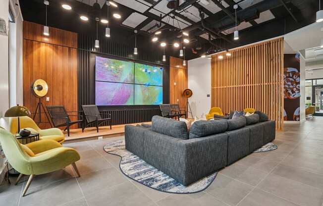 A modern living room with a grey sofa, a yellow chair, and a large screen on the wall.