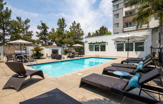 A pool with lounge chairs and umbrellas in front of a building.