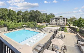 A large swimming pool surrounded by a black fence and lounge chairs.